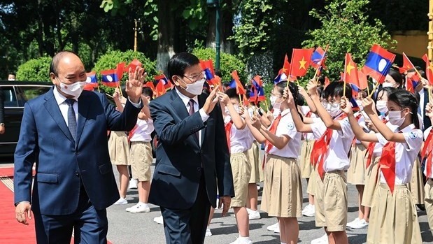 Vietnamese President Nguyen Xuan Phuc (L) and General Secretary of the Lao People’s Revolutionary Party Central Committee and President of Laos Thongloun Sisoulith wave hands at children at the welcome ceremony in Hanoi on June 28. (Photo: VNA)