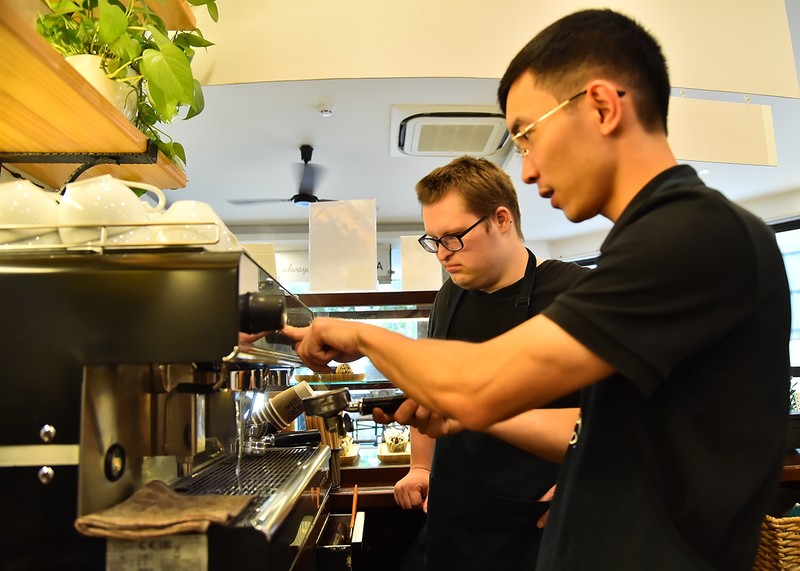 Tran Duc Thang, a staff member at Simple Coffee, introducing Evan to the store's coffee machine features and usage.