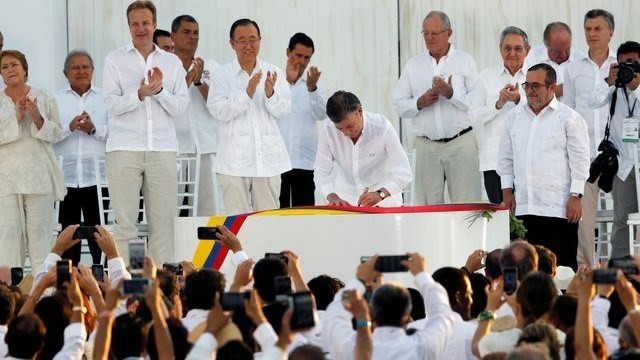 Colombian President Juan Manuel Santos (C) signs an accord ending a half-century war that killed a quarter of a million people, as Marxist rebel leader Rodrigo Londono (front, R), known by his nom de guerre Timochenko, looks on in Cartagena, Colombia, September 26, 2016. (Credit: Reuters)
