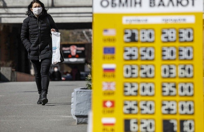 A woman wears a face mask amid concerns over the spread of the COVID-19 coronavirus. She passes by a currency exchange on March 25, 2020, in Kyiv showing the hryvnia weakening against the USD. (File photo: Kyiv Post)